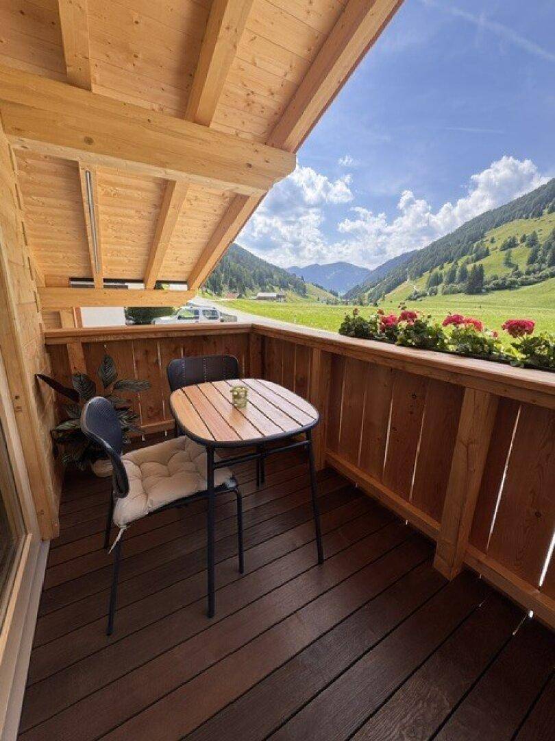 Gemütlicher Balkon mit Holzboden und Sitzgelegenheiten, bietet einen weiten Bergblick.