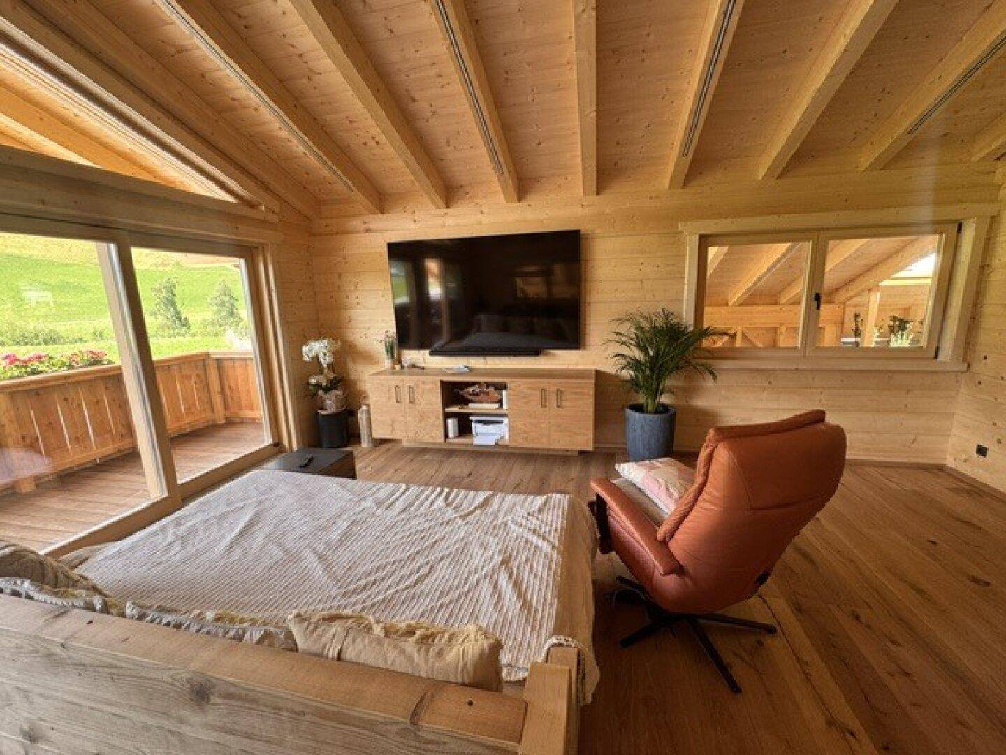 Heller Wohnbereich mit Holzboden, großem Fenster und Zugang zum Balkon.