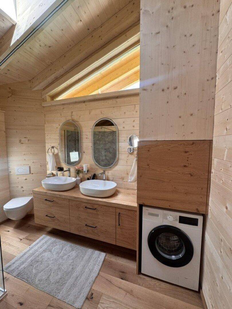 Helles Badezimmer mit Doppelwaschbecken, Waschmaschine und Holzelementen.