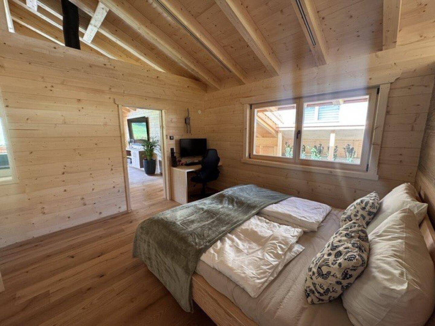 Helles Schlafzimmer mit Holzwänden, Schreibtisch und Blick auf die Umgebung.