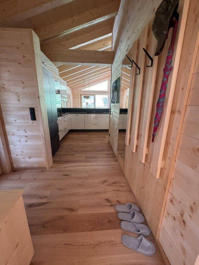 Heller Eingangsbereich mit Holzböden und -wänden, der zu einer modernen Küche führt.