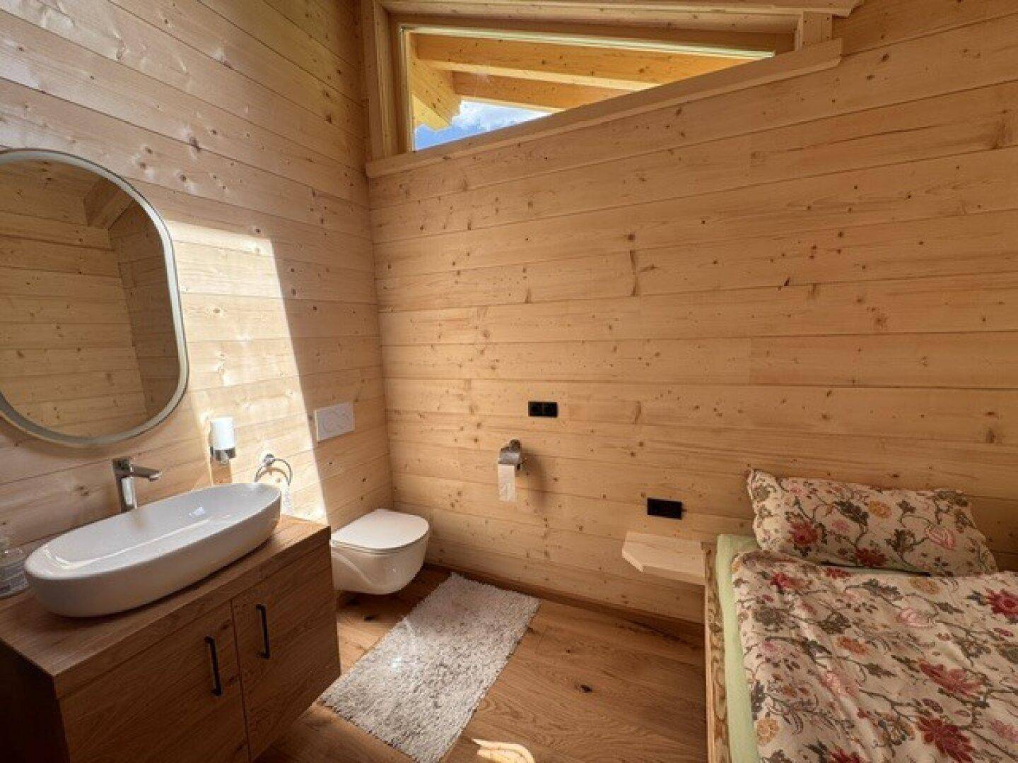Rustikales Schlafzimmer mit Holzausstattung, Einzelbett, Waschbecken und Toilette unter einem Dachfenster.