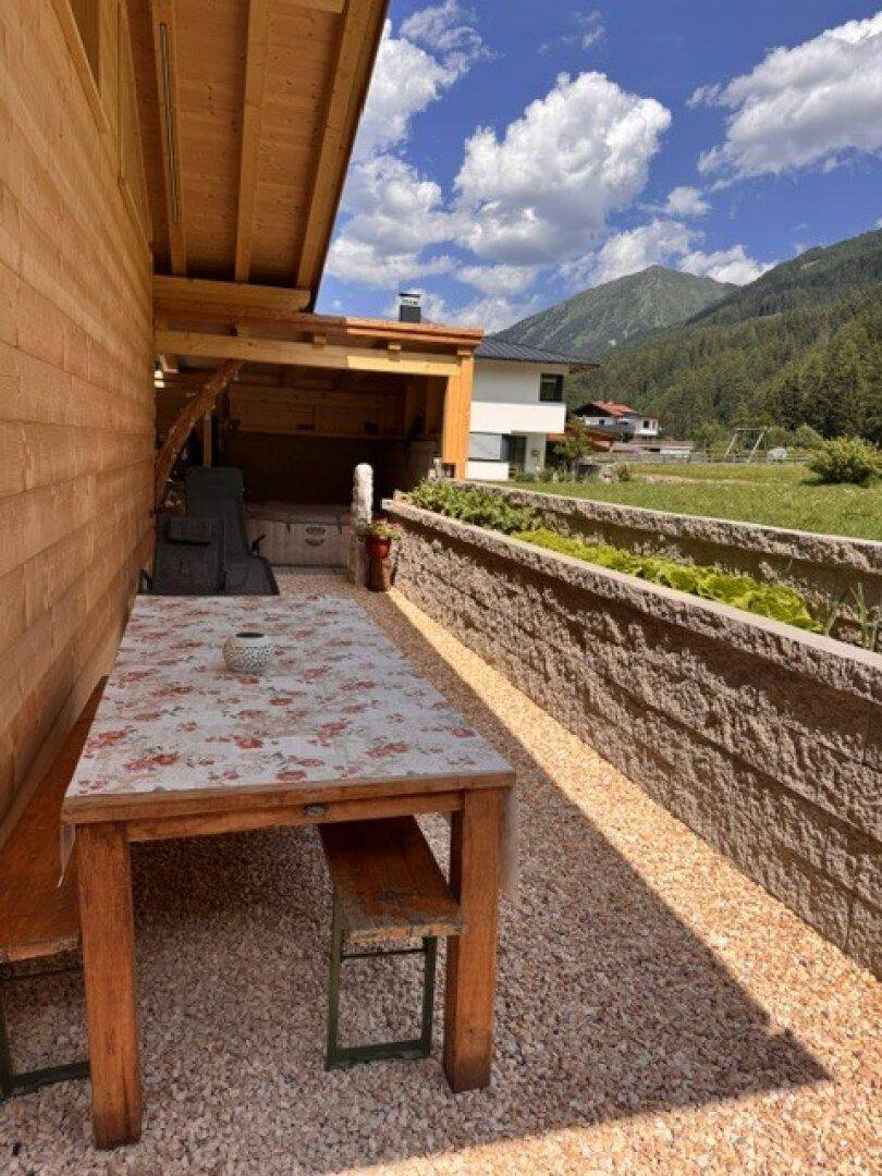 Gemütlicher Essbereich im Freien mit Holztisch, Bänken und Blick auf die umliegende Bergwelt.