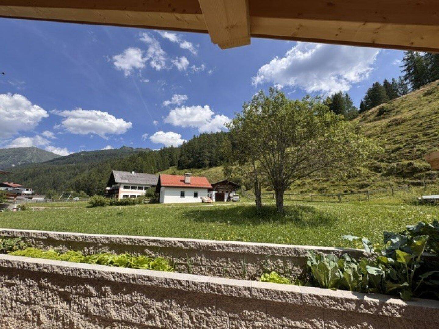 Weitläufiger Blick von der Terrasse über grüne Wiesen, Häuser und majestätische Berge.