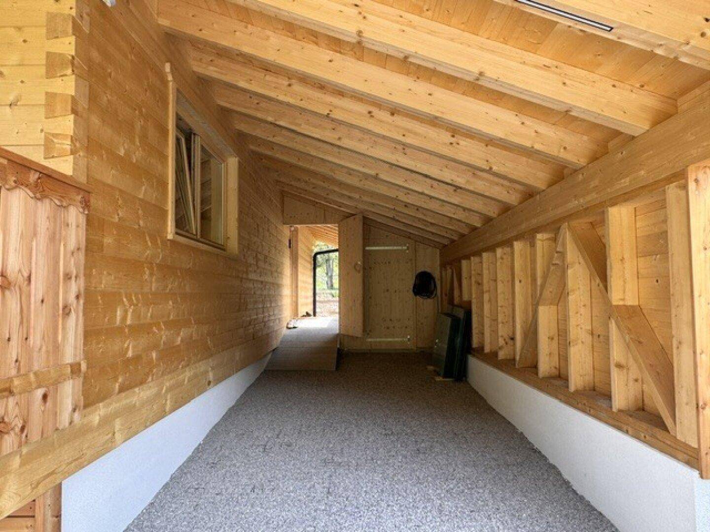 Überdachter Carport-Bereich mit Holzwänden und Kiesboden, führt zum Eingang des Hauses.