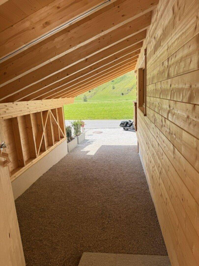 Überdachter Zugangsbereich mit Holzwänden und Blick auf die grüne Landschaft und Straße.