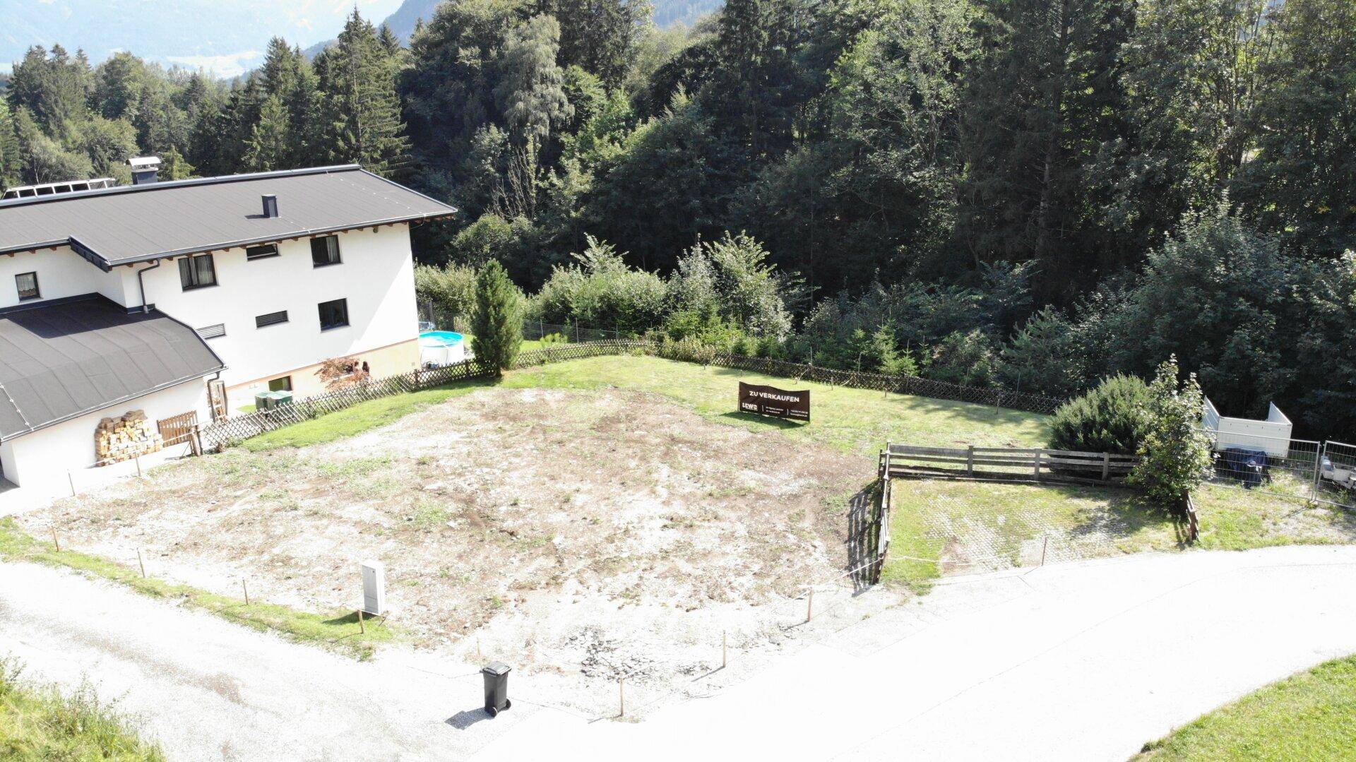 Weitläufiges Baugrundstück aus der Vogelperspektive, umgeben von Bäumen und einem Nachbarhaus mit Pool.