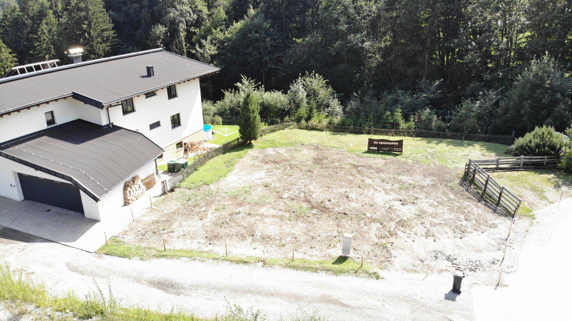 Luftaufnahme eines Baugrundstücks mit angrenzendem Haus, Garage und einem "ZU VERKAUFEN" Schild.