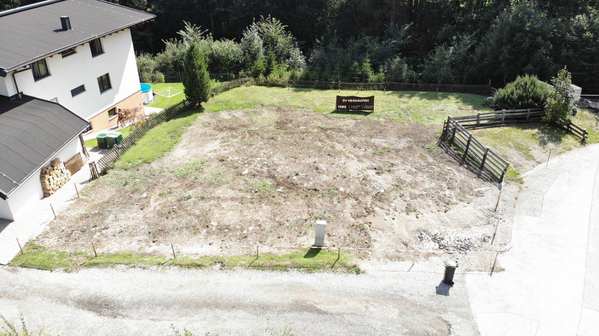 Weitläufiges Baugrundstück aus der Vogelperspektive, umgeben von Bäumen und einem Nachbarhaus mit Pool.