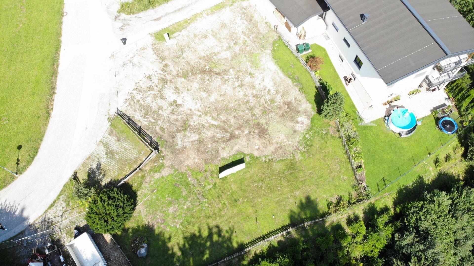 Draufsicht auf ein Baugrundstück mit angrenzendem Haus, Pool und Trampolin, umgeben von Natur.