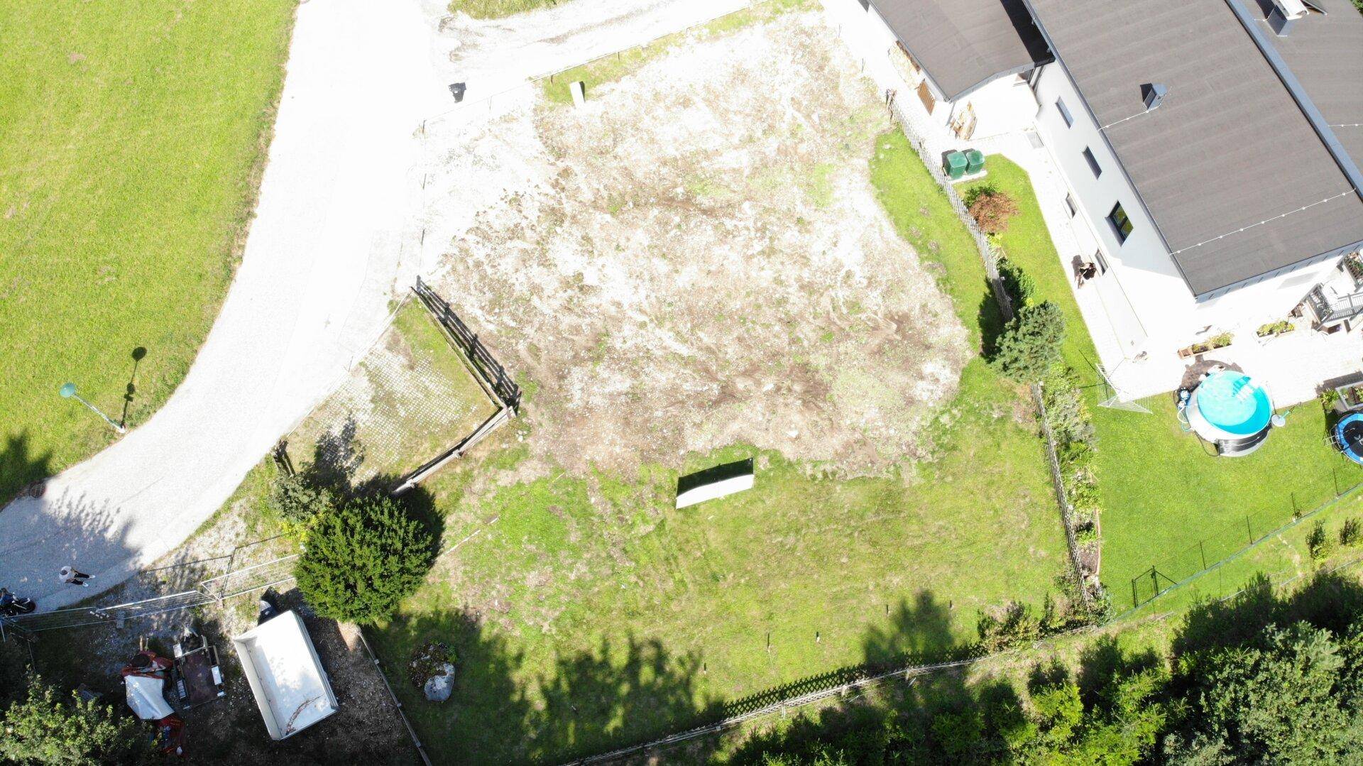Draufsicht auf ein Baugrundstück mit angrenzendem Haus, Pool und Trampolin, umgeben von Natur.