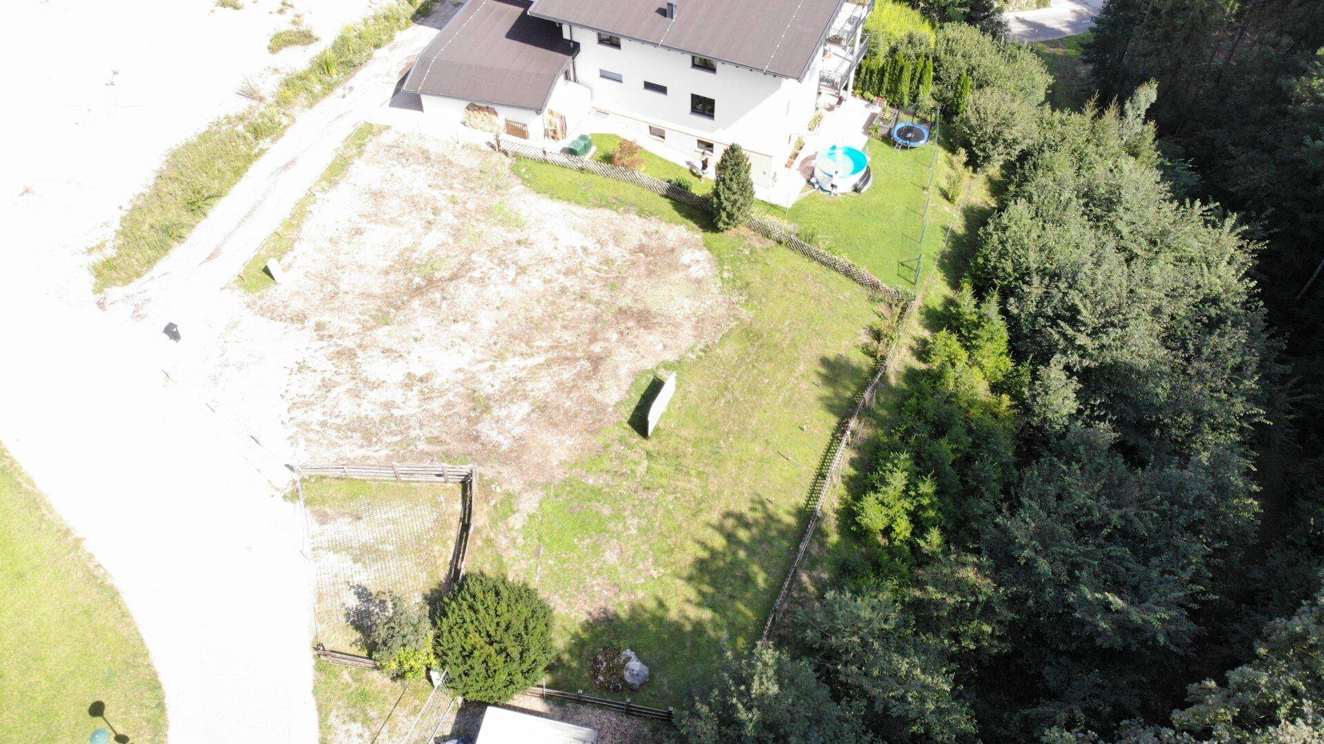 Vogelperspektive eines Baugrundstücks, umgeben von dichtem Wald und einem angrenzenden Wohnhaus.