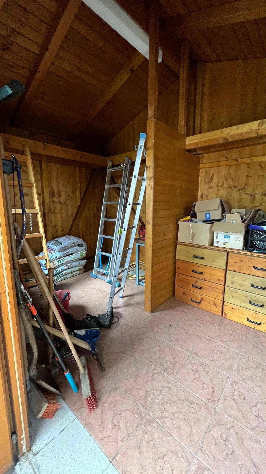 Innenansicht des Holzschuppens mit Werkzeugen, Leitern und Stauraum.