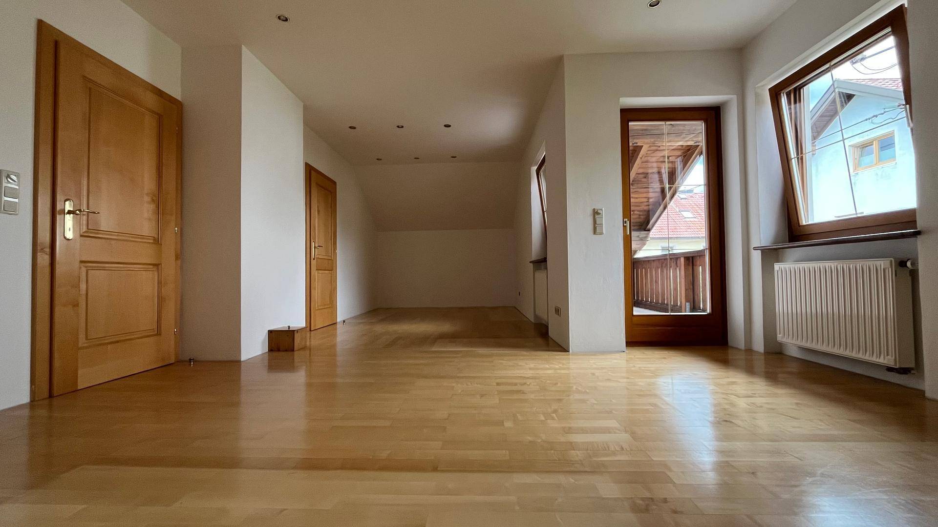Helles Zimmer im Dachgeschoss mit Parkettboden, Holztüren und Balkonzugang.