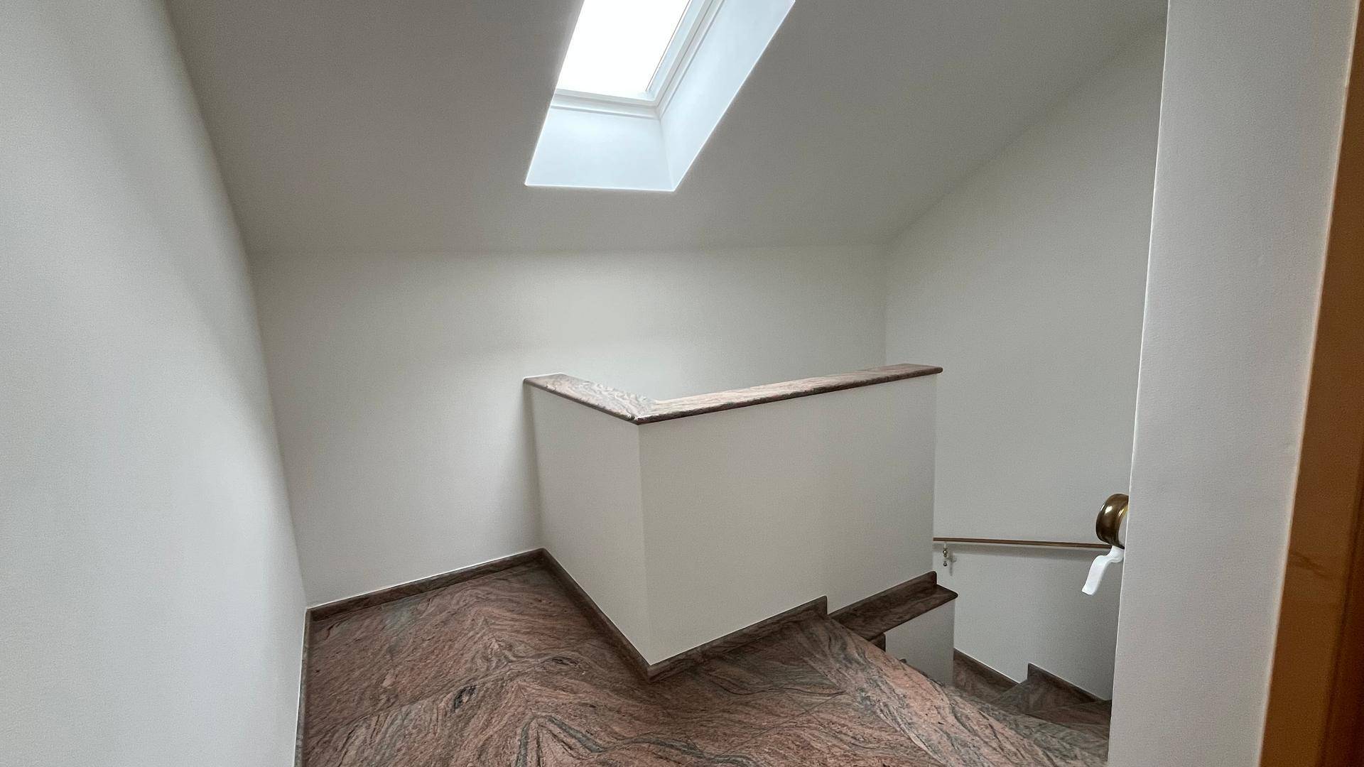 Treppenhaus mit Marmorstufen, weiß gestrichenen Wänden und einem Oberlicht für natürliches Licht.