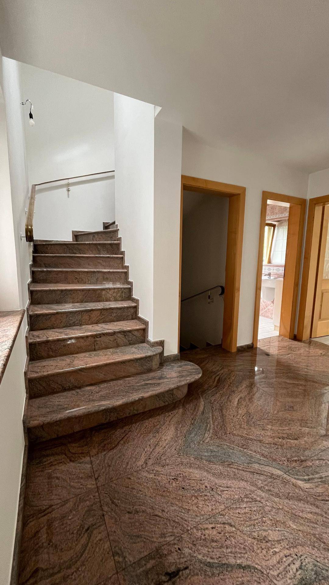 Eingangsbereich mit breiter Steintreppe und glänzendem Marmorboden in warmen Rottönen.
