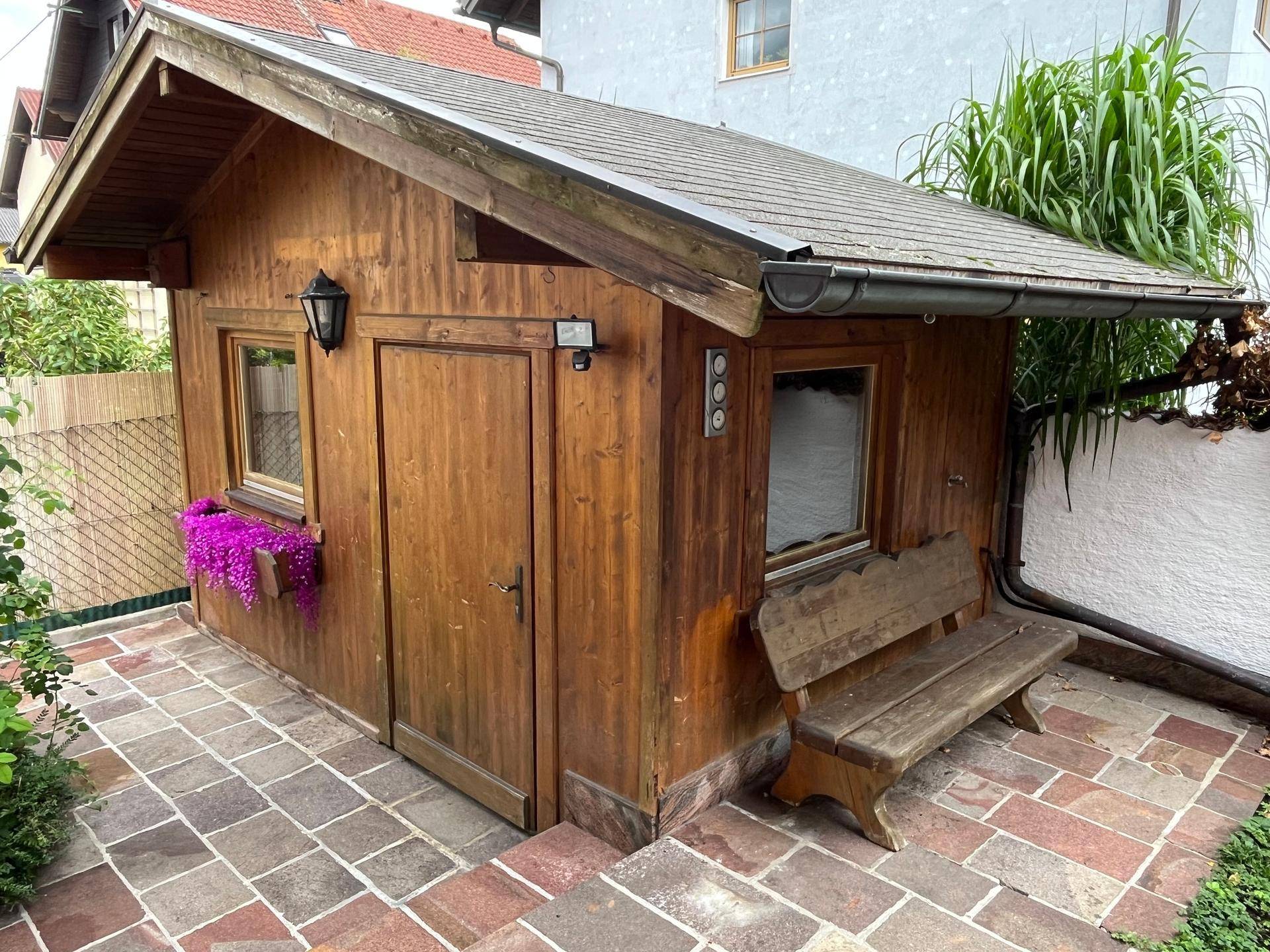 Rustikaler Holzschuppen im Garten mit Sitzbank und Blumenkästen.