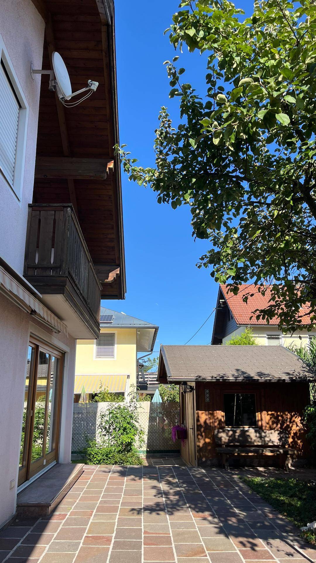 Terrasse mit Steinplatten, umgeben von Bäumen und einem kleinen Holzschuppen im Garten.