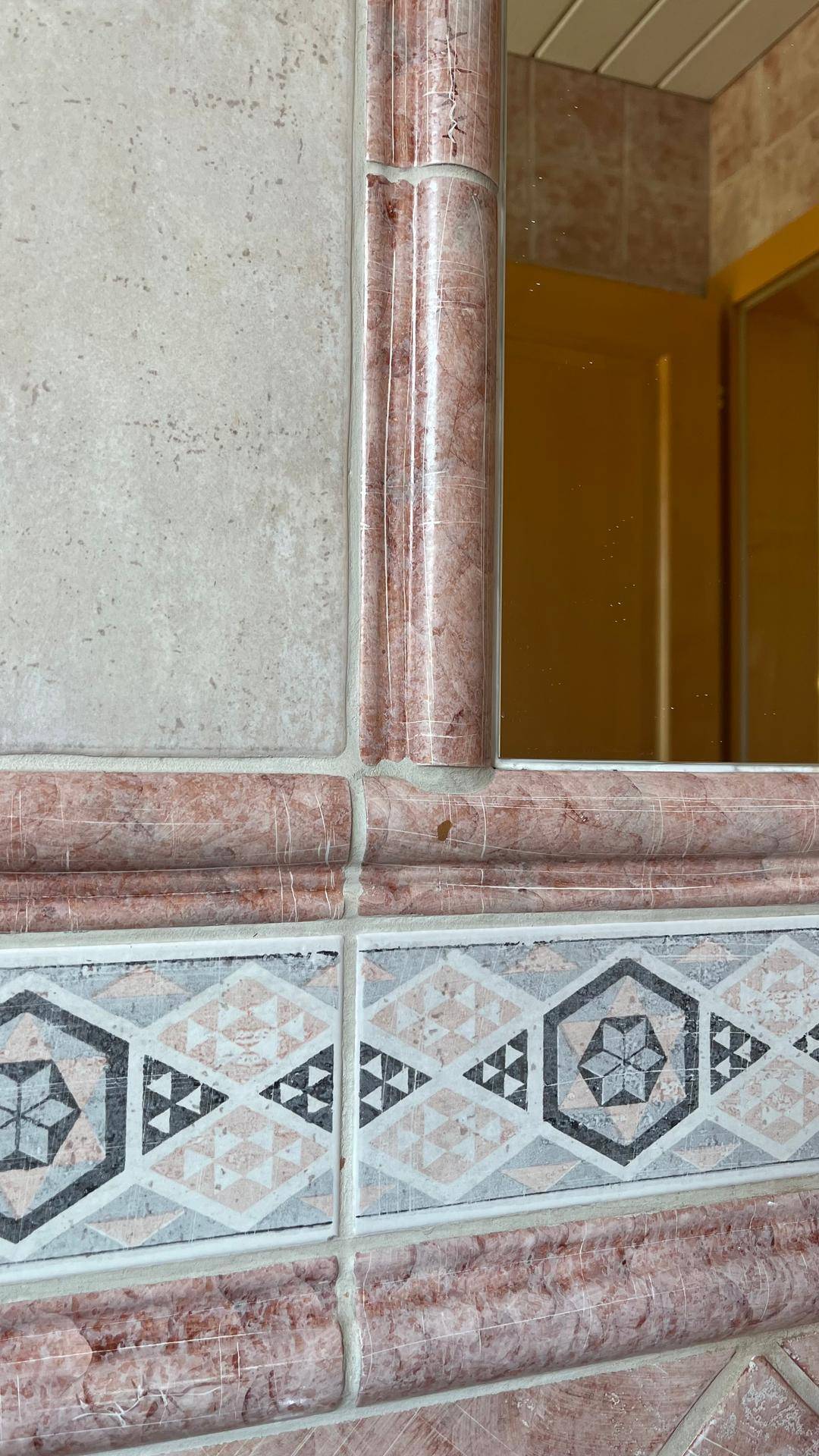 Nahaufnahme von Wandfliesen mit geometrischen Mustern und einem Spiegel.