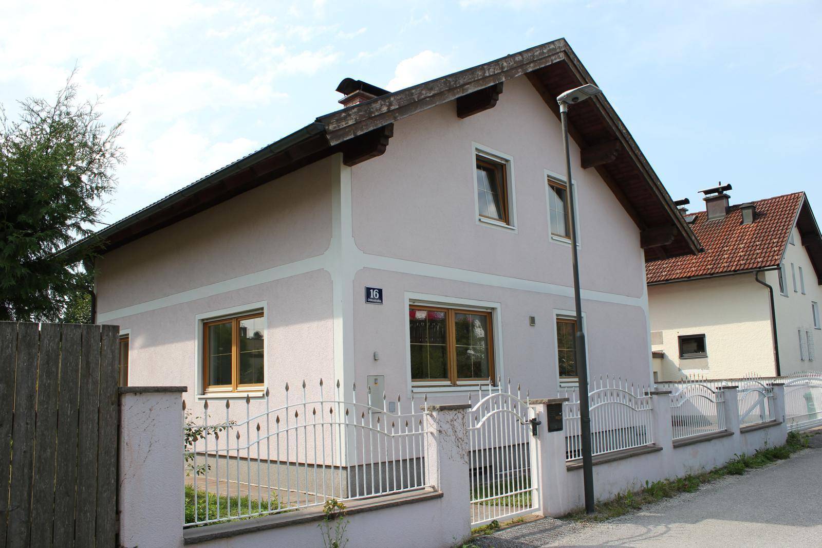 Ansicht des Einfamilienhauses von der Straßenseite mit hellrosa Fassade und Vorgarten.