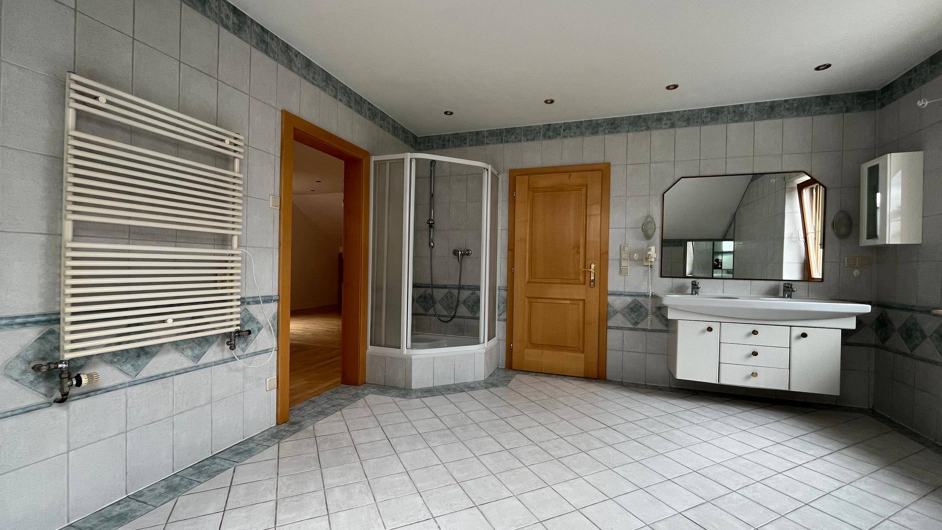 Geräumiges Badezimmer mit Duschkabine, beheiztem Handtuchhalter und Fliesenboden.