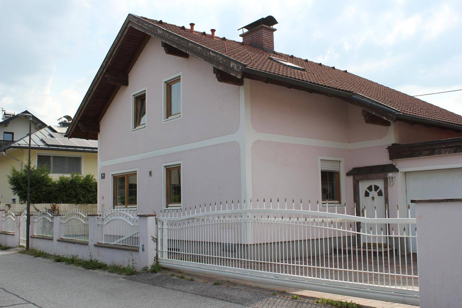 Einfamilienhaus mit hellrosa Fassade, weißem Zaun und traditionellem Satteldach.