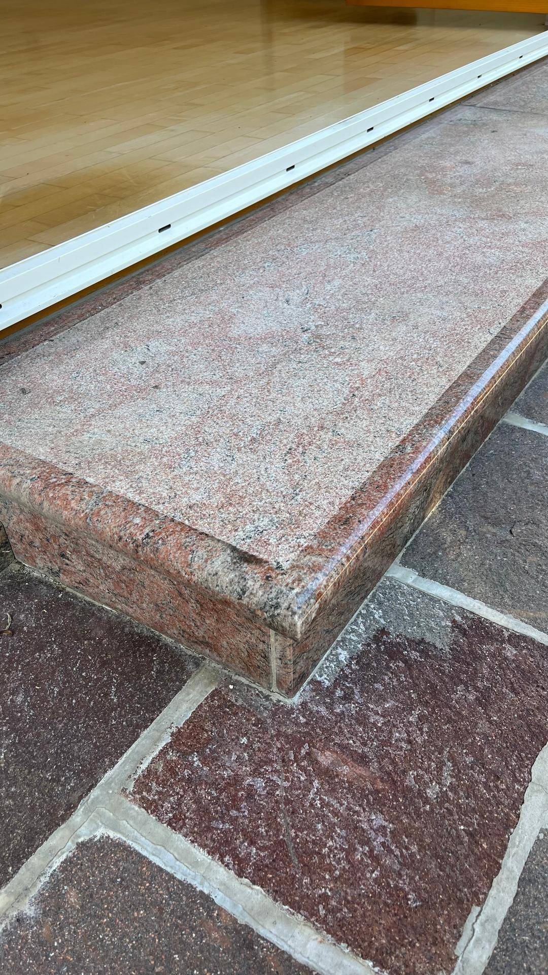 Detailaufnahme einer Granitstufe, die zu einer gepflasterten Terrasse führt.