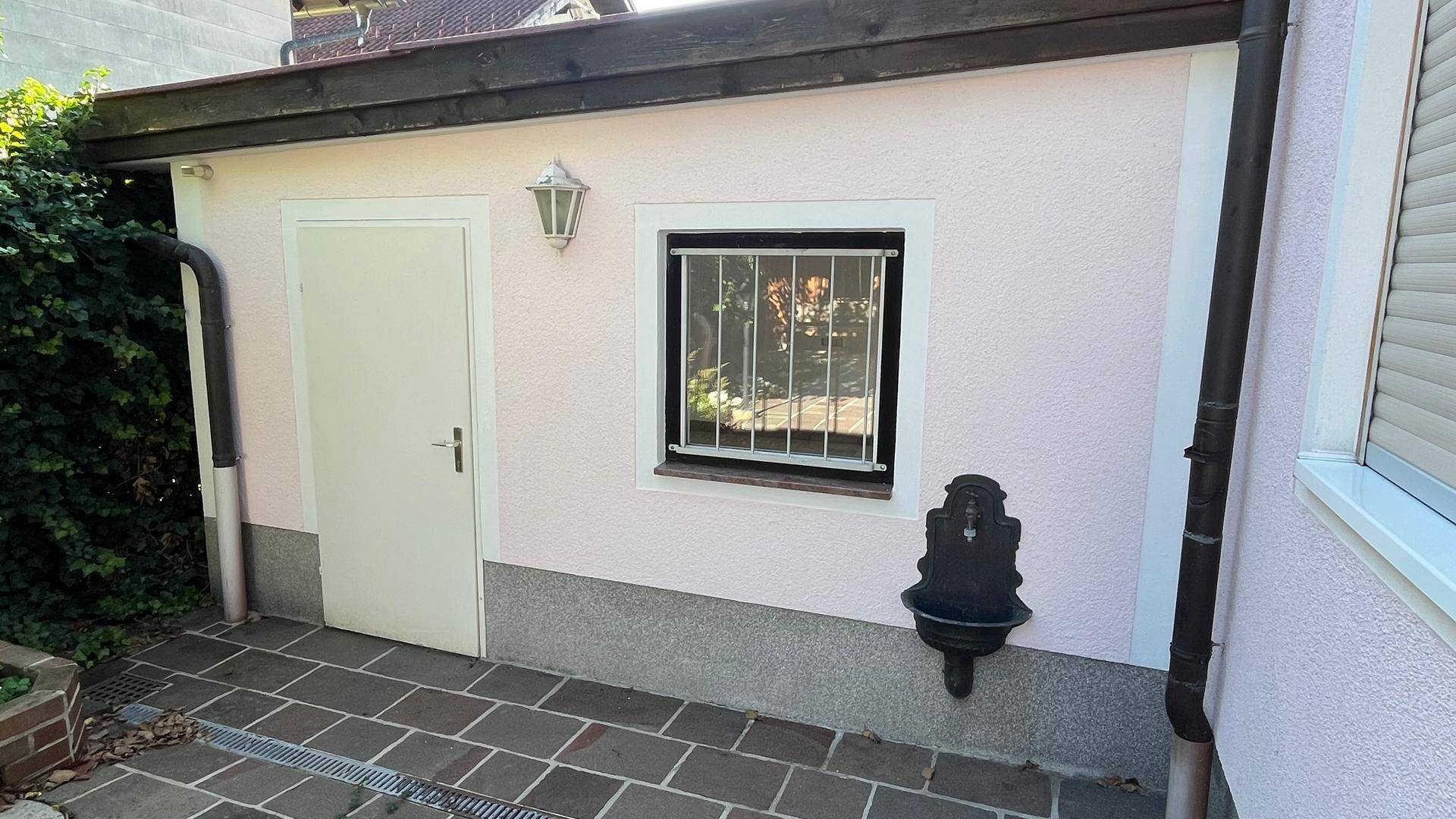 Seitenbereich des Hauses mit einer Tür, Fenster und einem Außenwasserhahn.