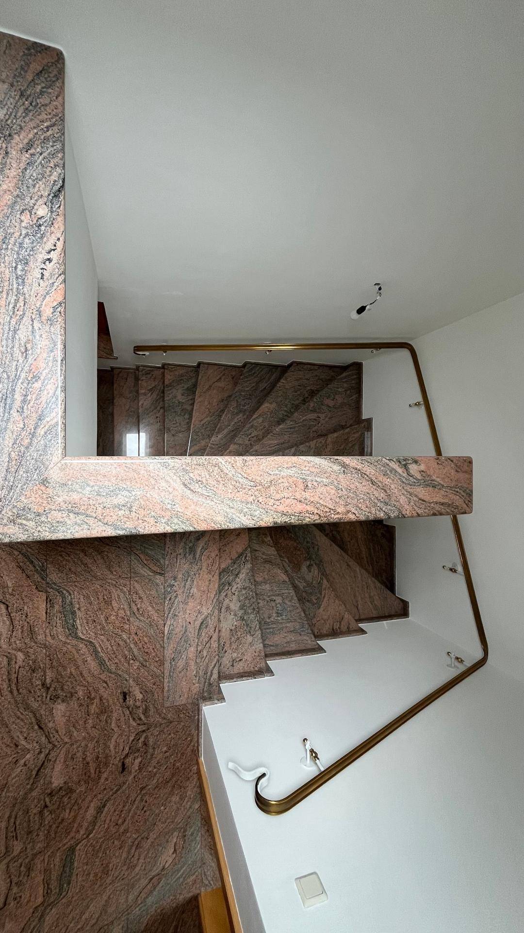 Blick von oben auf die geschwungene Marmortreppe mit elegantem Messinggeländer.