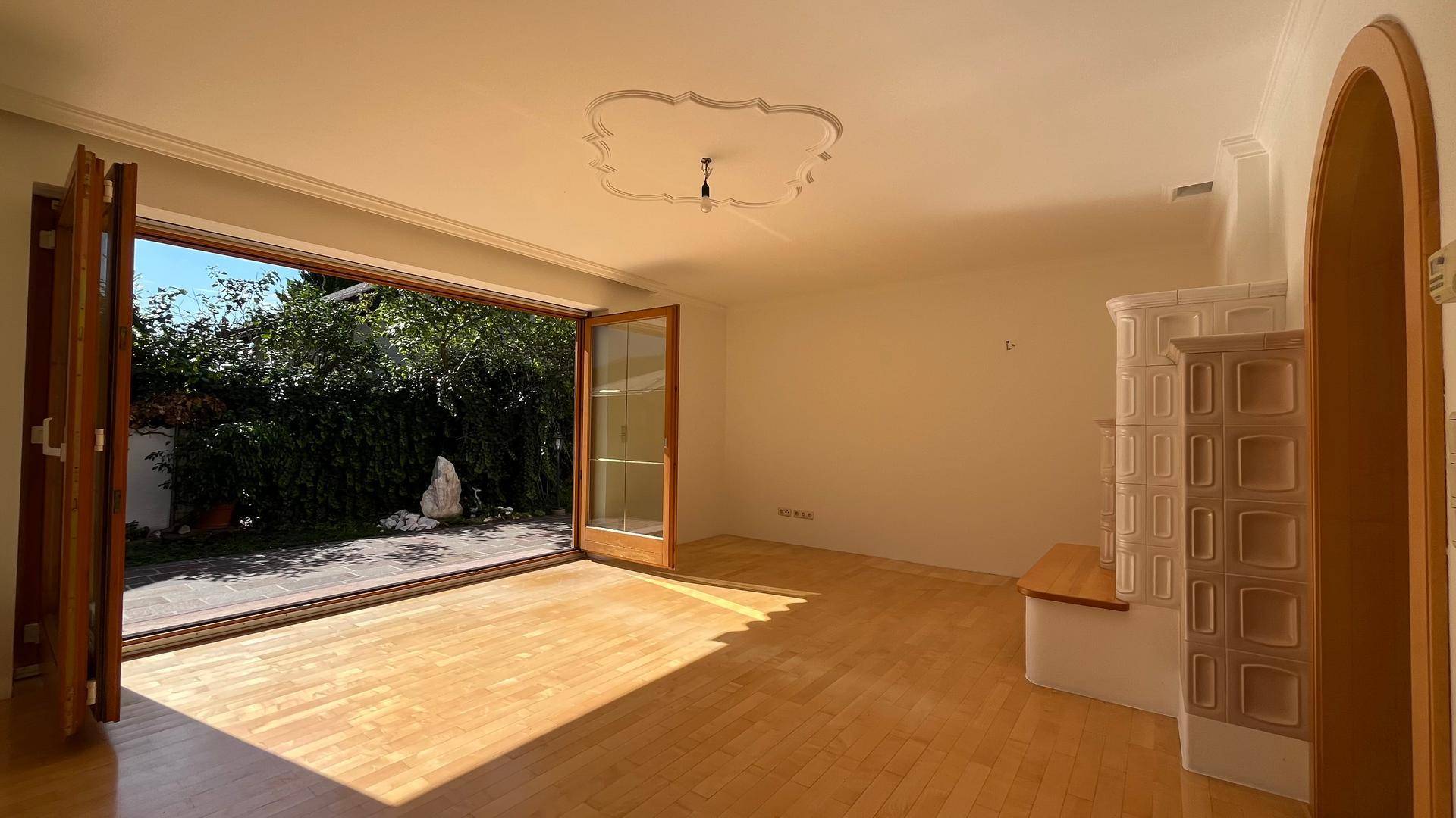 Geräumiges Wohnzimmer mit Parkettboden, Kachelofen und Zugang zur Terrasse.
