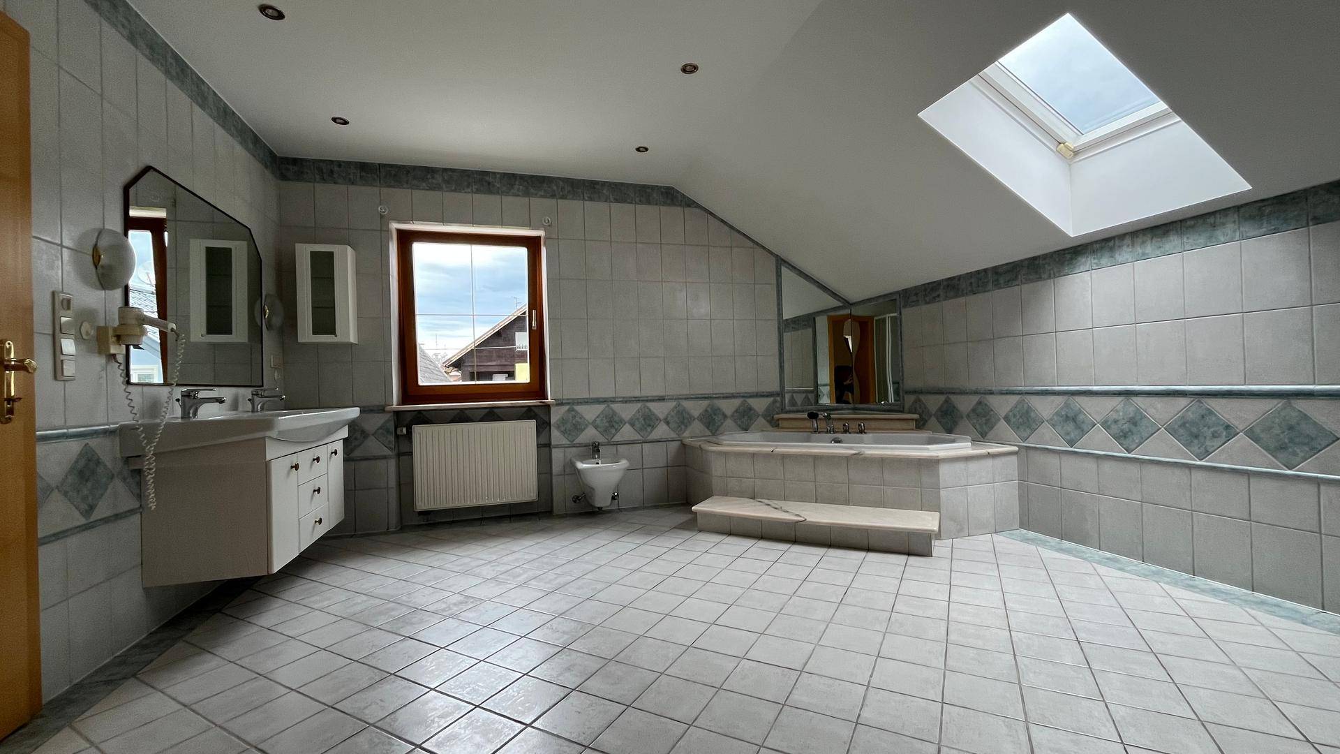 Großes Badezimmer mit Fliesenboden, Eckbadewanne, Doppelwaschbecken und Dachfenster.
