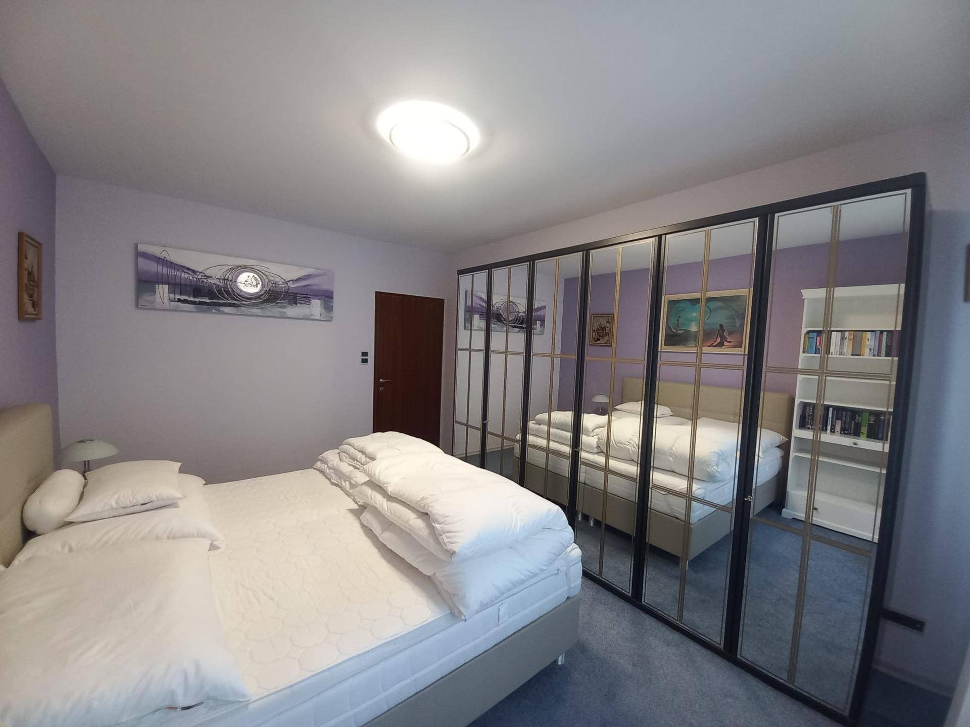 Schlafzimmer mit lila Wänden, einem bequemen Doppelbett und einem großen Spiegelschrank, der den Raum erweitert.