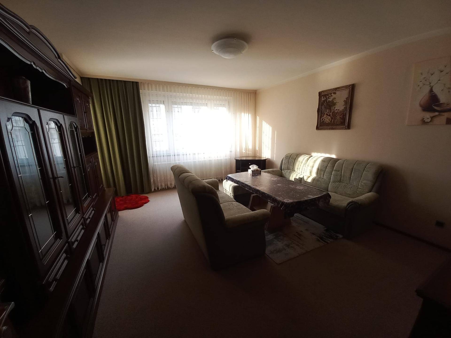 Helles Wohnzimmer mit beigen Wänden, bequemen Sofas und einem großen Holzschrank, der Stauraum bietet.