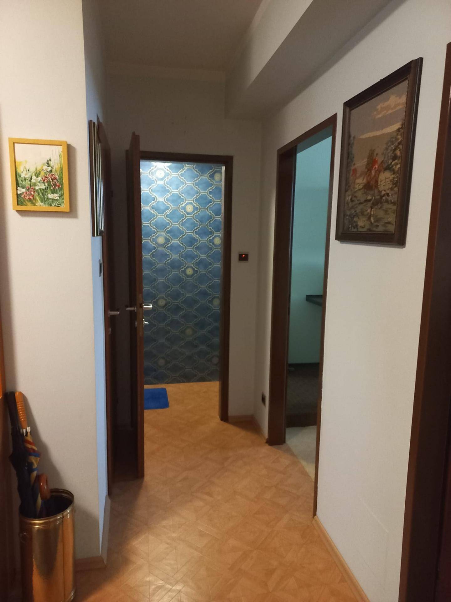Flur mit hellem Fliesenboden und Blick in ein Zimmer mit auffälliger blauer Tapete durch eine offene Tür.