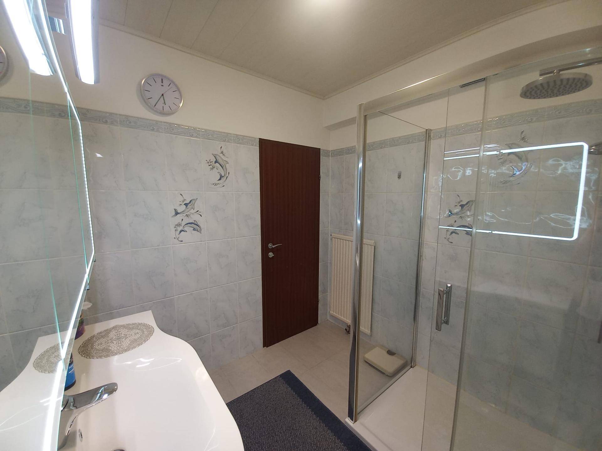 Badezimmer mit hellblauen Fliesen, einer Duschkabine und einem Heizkörper, der für Komfort sorgt.