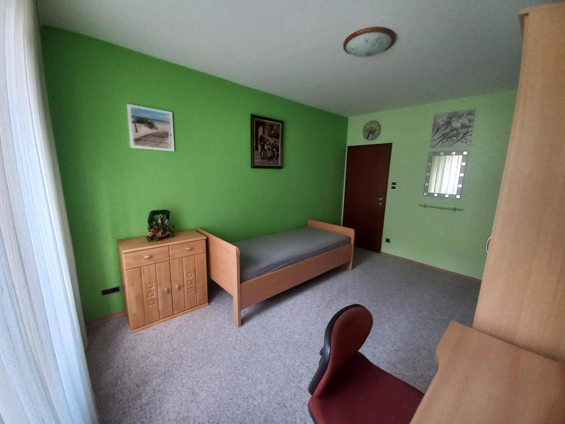 Helles Schlafzimmer mit lebhaften grünen Wänden, einem Einzelbett und einem Nachttisch aus hellem Holz.