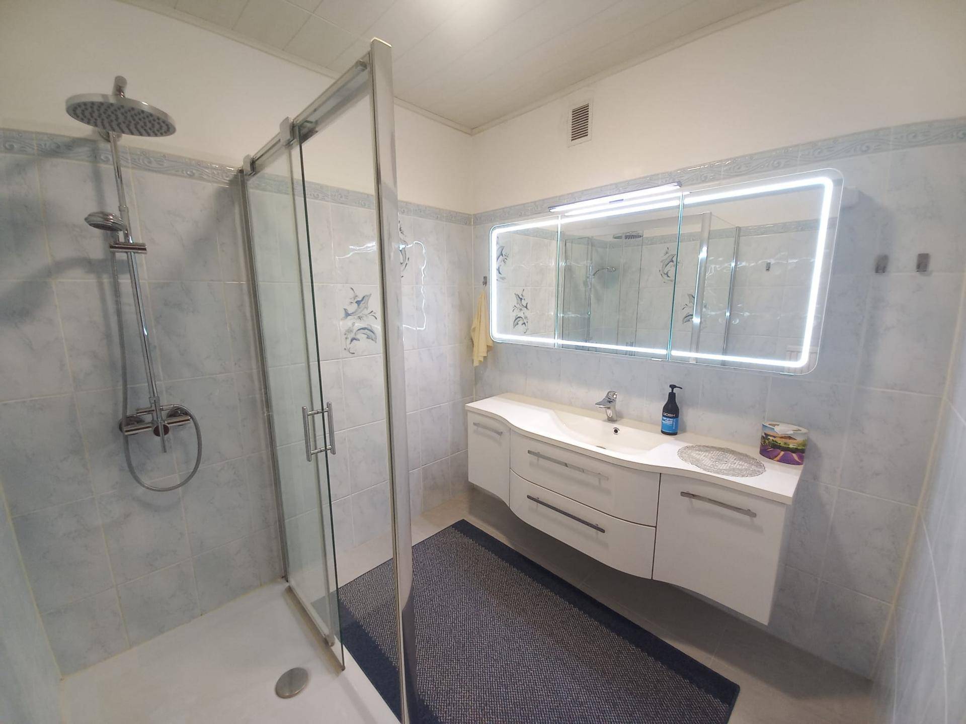 Modernes Badezimmer mit einem eleganten Waschtisch, beleuchtetem Spiegelschrank und einer geräumigen Duschkabine.