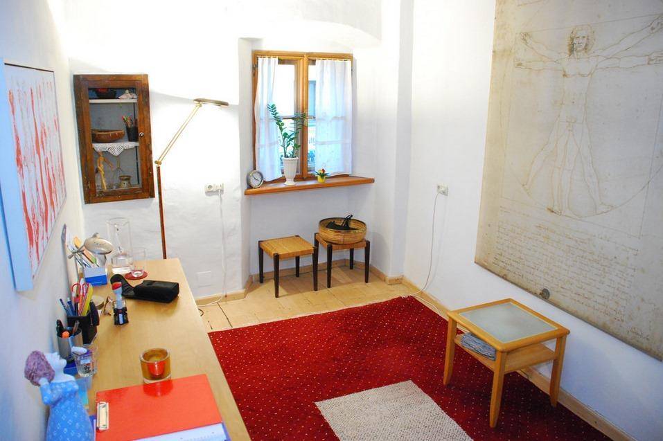 Kleines Arbeitszimmer mit Schreibtisch, Fenster und einem großen Kunstwerk an der weißen Wand.