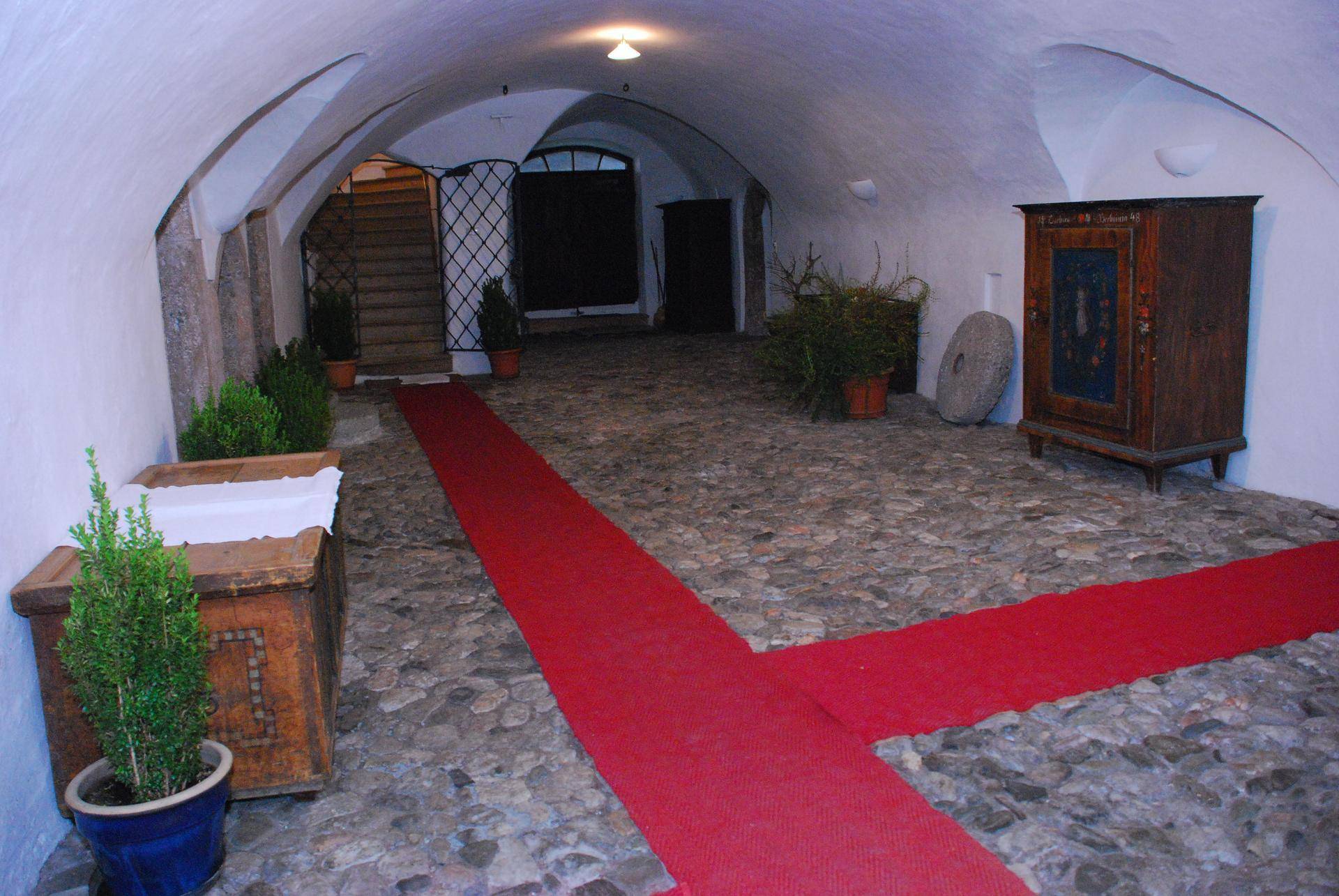 Historischer Eingangsbereich mit Gewölbedecke, Kopfsteinpflasterboden und einem roten Teppich.
