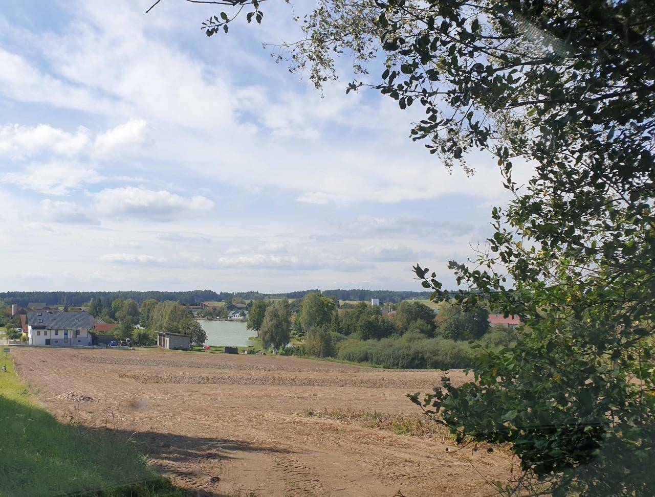 Weitläufiger Blick über Felder, einen See und die ländliche Umgebung mit vereinzelten Häusern.