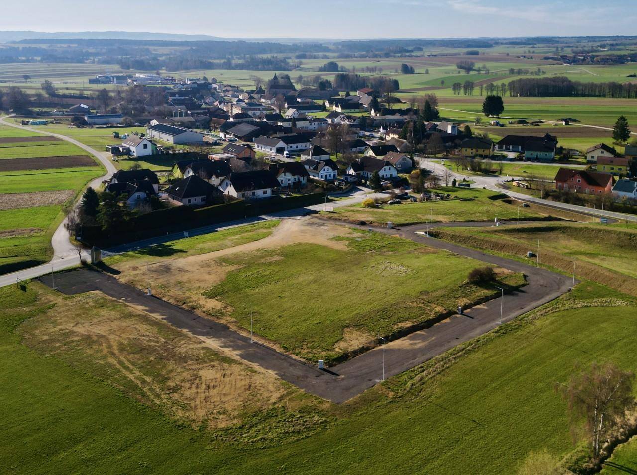 Luftaufnahme eines großen unbebauten Grundstücks mit grüner Wiese, umgeben von Feldern und einem Dorf in der Ferne.