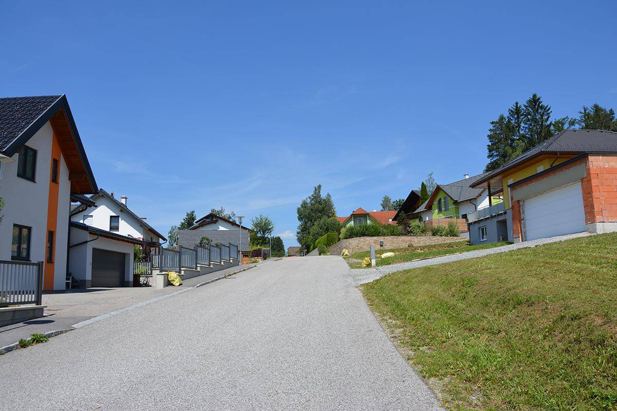 Eine Wohnstraße mit verschiedenen Häusern, teils im Bau, teils fertiggestellt, umgeben von grüner Landschaft.