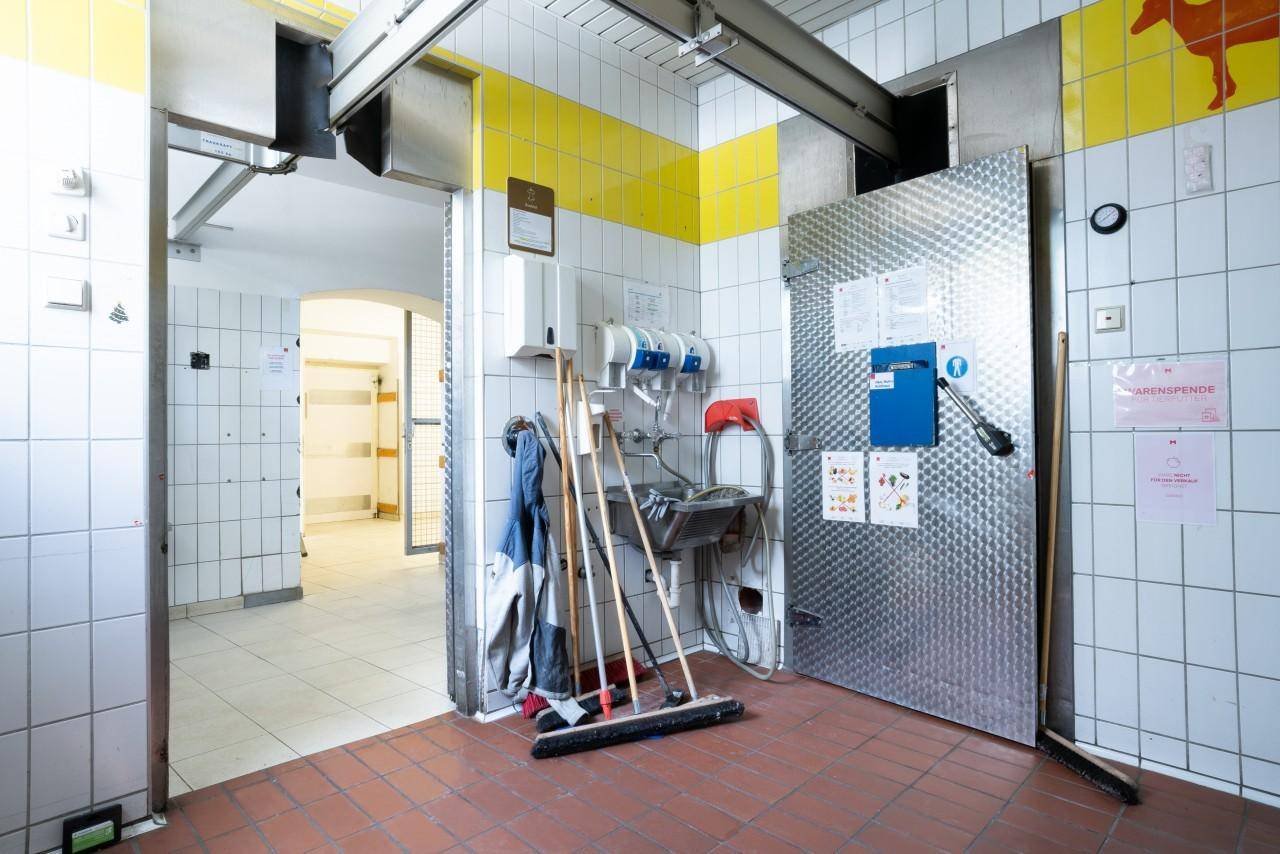 Funktionaler Nebenraum mit Waschbecken, Reinigungsgeräten und gefliesten Wänden.
