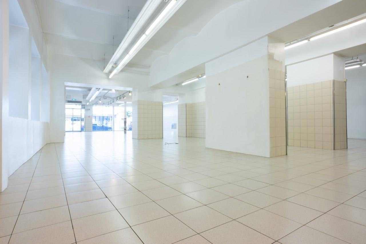 Heller Verkaufsraum mit großen Fenstern zur Straße und weiß gefliestem Boden.
