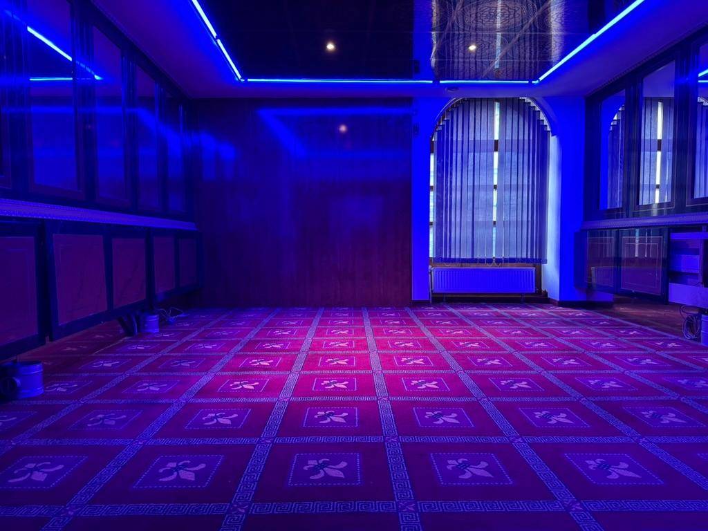 Geräumiger Veranstaltungsraum mit rotem Teppich, blauer LED-Beleuchtung und Fenstern mit Jalousien.