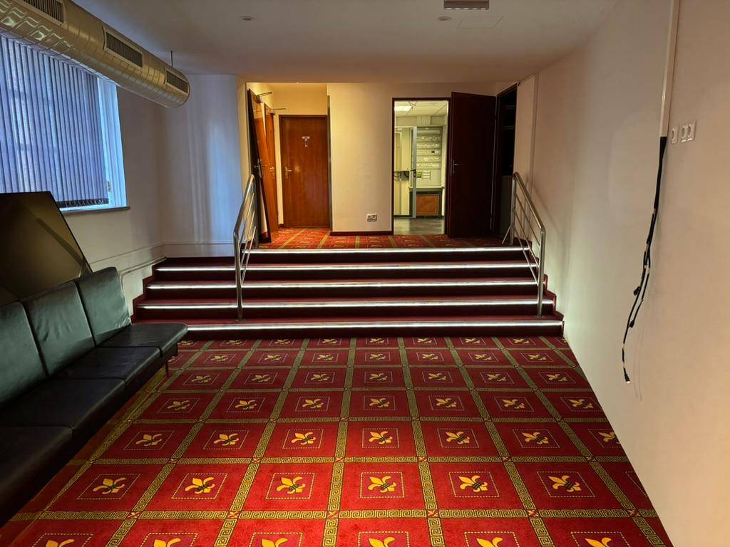 Flur mit beleuchteter Treppe, rotem Teppich und einer Sitzgelegenheit.