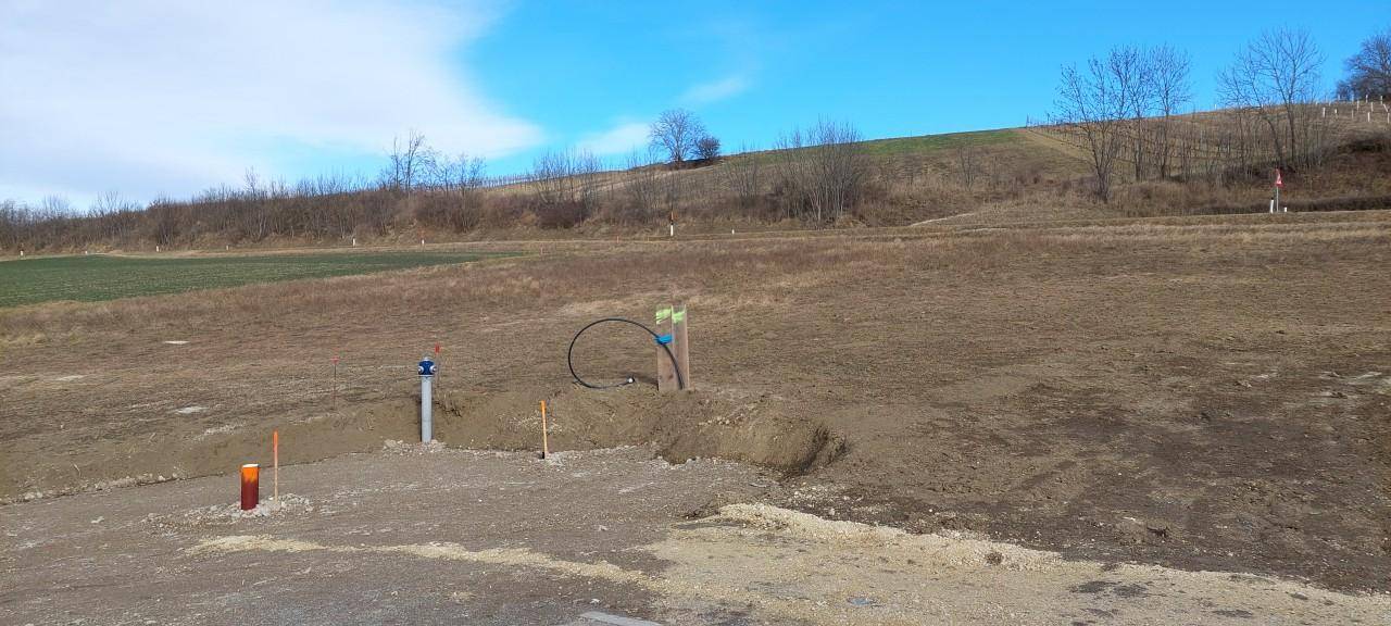 Unbebautes Grundstück in ländlicher Umgebung mit vorbereiteten Anschlüssen für den Neubau und Blick auf Hügel.