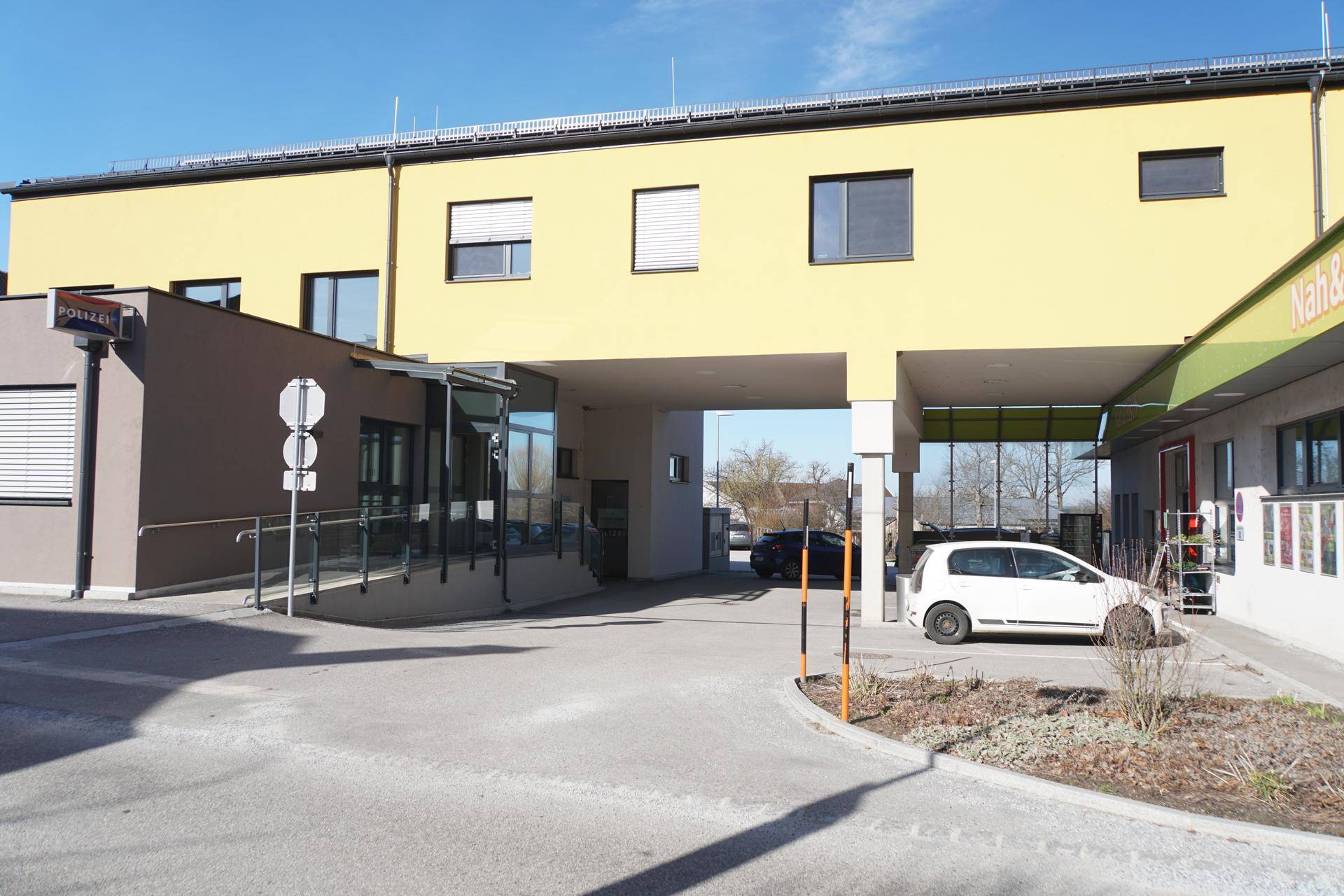 Modernes gelbes Geschäftsgebäude mit Parkplätzen, Zufahrt und einer barrierefreien Rampe.