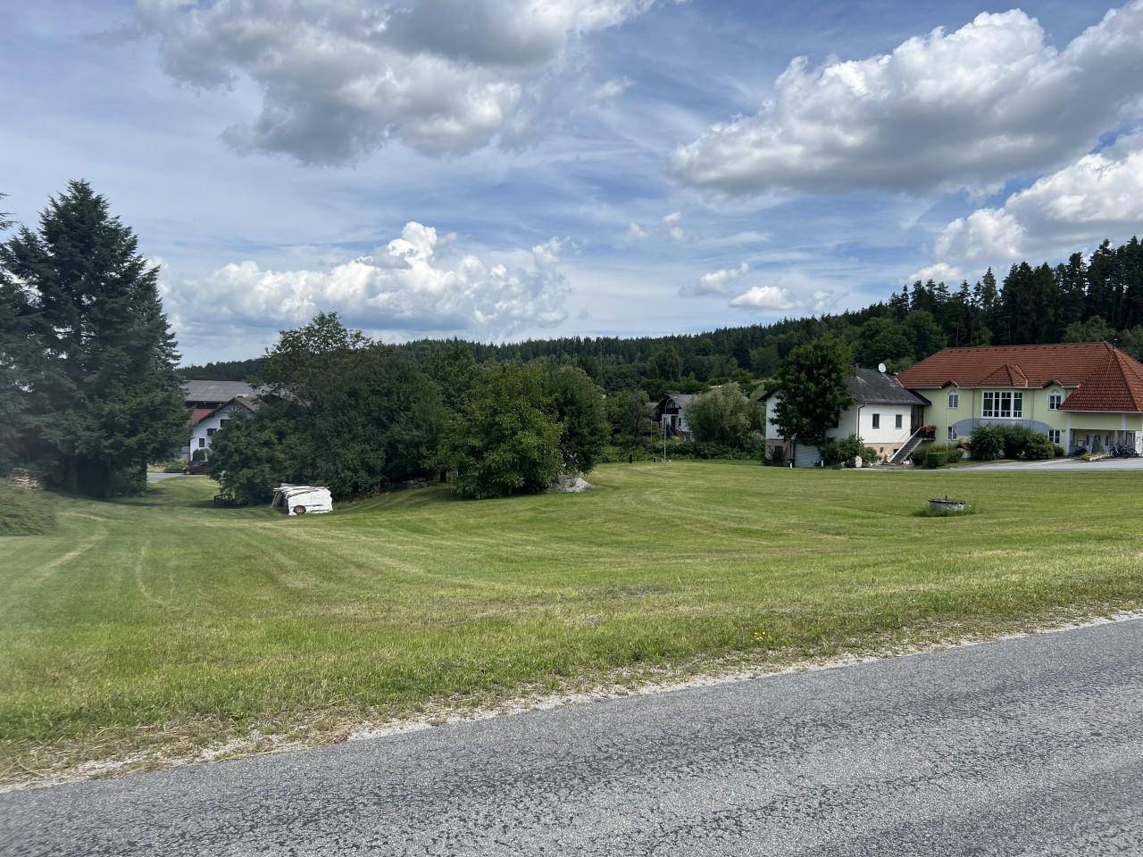 Panoramablick auf ein Wohnhaus mit weitläufiger Grünfläche und bewaldeter Hügellandschaft im Hintergrund.