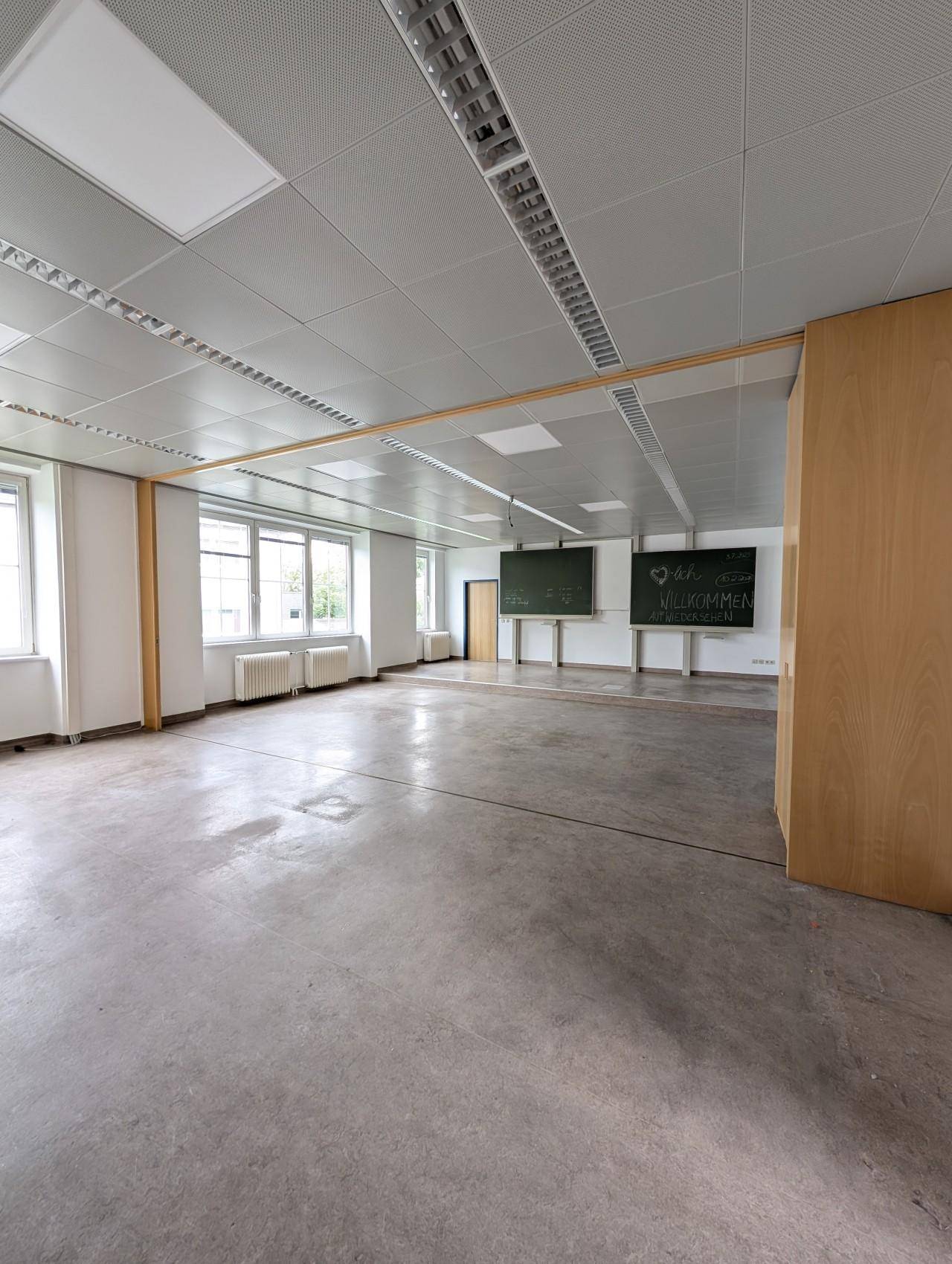 Heller, geräumiger Raum mit Linoleumboden, abgehängter Decke und Tafeln an der Wand.